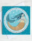 A nautical greetings card featuring a swimming mermaid as seen through a ships porthole.