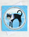 A nautical greetings card featuring a black cat in a sailor hat peeking through a ships porthole.
