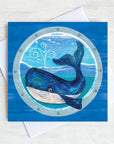 A nautical greetings card featuring a big blue whale as seen through a ships porthole.