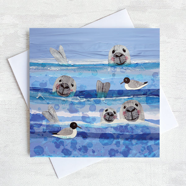A greetings card featuring 3 seals heads bobbing in the sea amongst the black headed gulls.