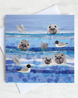 A greetings card featuring 3 seals heads bobbing in the sea amongst the black headed gulls.