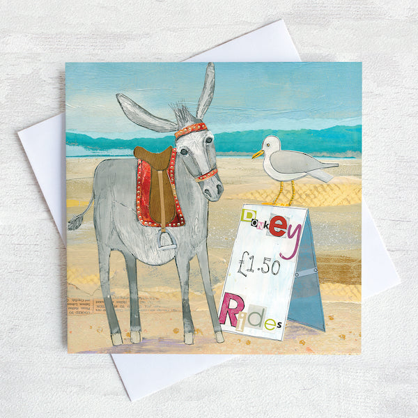 A coastal greetings card featuring a seaside donkey chatting to a seagull who is sitting on top of a sign advertising Donkey rides.