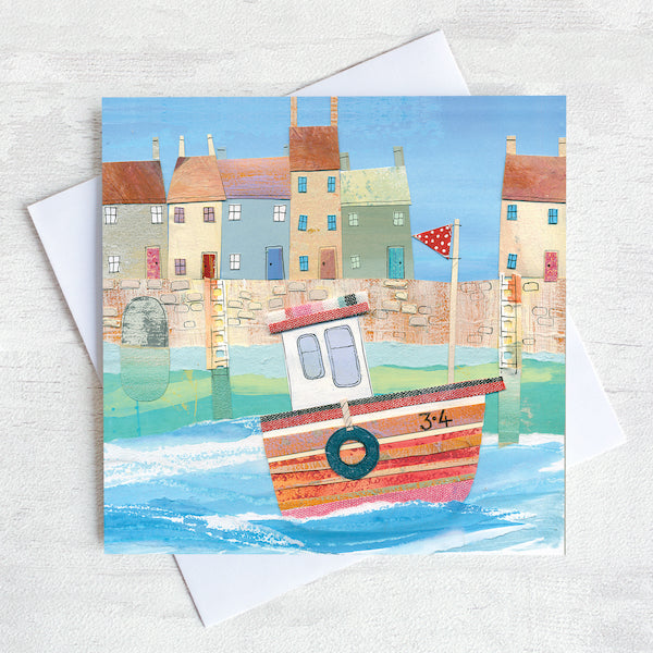 A charming coastal greetings card featuring a paper collage of a fishing boat in front of a row of colourful cottages in a harbour.