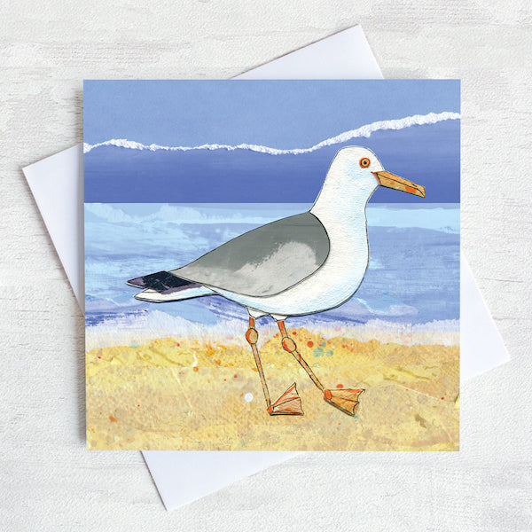 A greetings card featuring a seagull a yellow sandy beach.