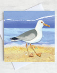 A greetings card featuring a seagull a yellow sandy beach.