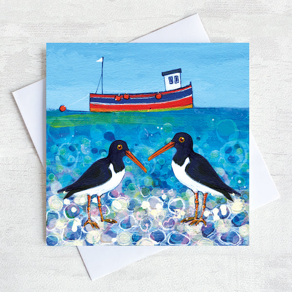A charming greetings card from an original painting by Joanne Wishart, these quirky oystercatchers chat on a pebbled beach with a cute little fishing boat bobbing on a teal green sea.