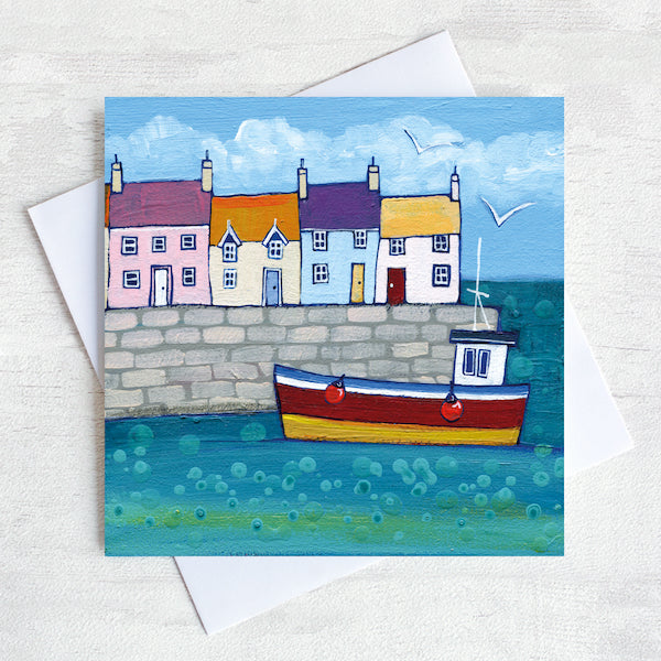 A charming coastal greetings card featuring colourful cottages on a harbour wall with a fishing boat bobbing in the water.
