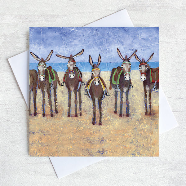 A coastal greetings card featuring a row of seaside donkeys on a beach.