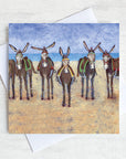 A coastal greetings card featuring a row of seaside donkeys on a beach.