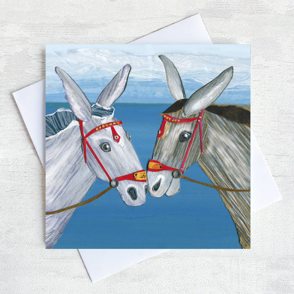 A nostalgic greetings card featuring two seaside donkeys rubbing noses on a beach.