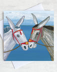 A nostalgic greetings card featuring two seaside donkeys rubbing noses on a beach.