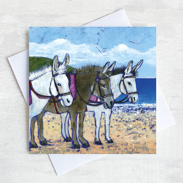 A greetings card featuring three fluffy seaside donkeys on a beach.