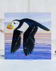 A flying puffin gliding over the sea in the evening light on a greetings card.