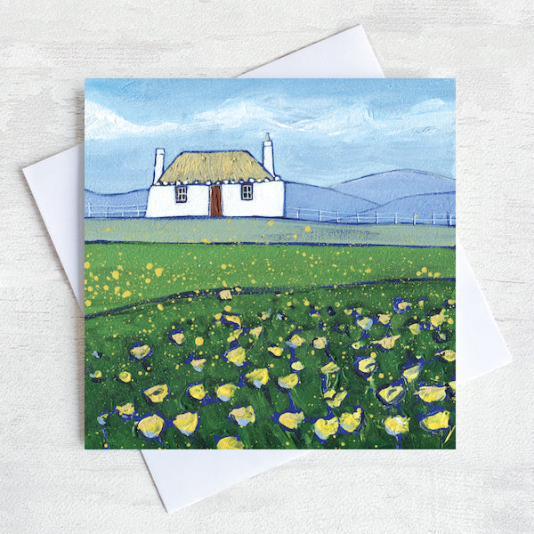 A greetings card featuring a scottish thatched cottage with a field of buttercups in the foreground.