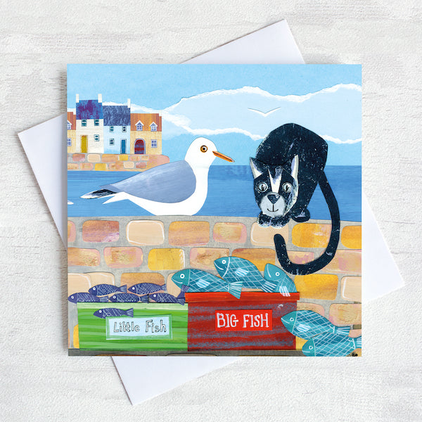 A coastal greetings card with a cute cat and seagull sitting on a harbour wall looking to eat the catch of the day 