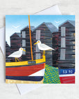 A charming seaside greetings card featuring a cute little harbour with seagulls perched on the cable boats infant of the net sheds.