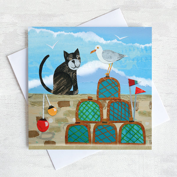 A coastal greetings card featuring a black cat in conversation with a cheeky seagull. They are on a harbour wall surrounded by lobster pots.