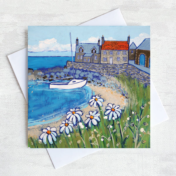 A greetings card featuring a colourful painting of craster harbour with daises in the foreground and a sailing boat in the bay.