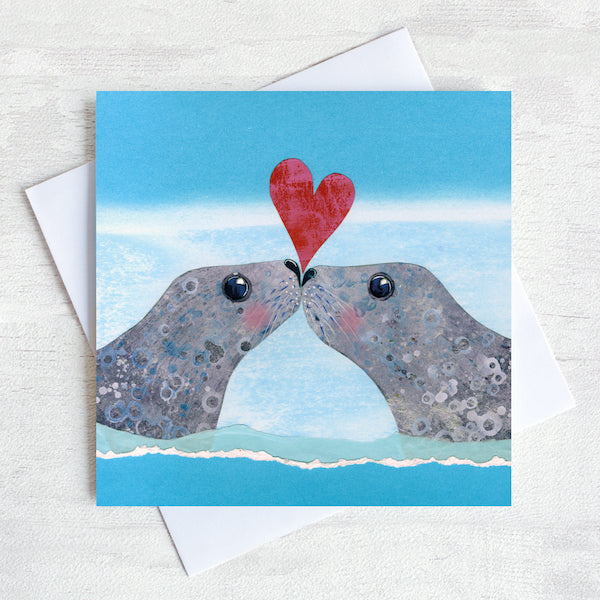 A valentines card featuring two seals kissing and a love heart .