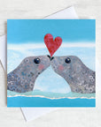 A valentines card featuring two seals kissing and a love heart .