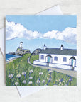 A greetings card featuring the white cottages and lighthouse on llanddwyn island on Anglesey with clover  flowers peppered in the foreground.