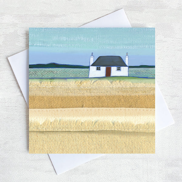 A greetings card featuring a traditional scottish blockhouse with a black roof and a red door. In front is a field of grass.