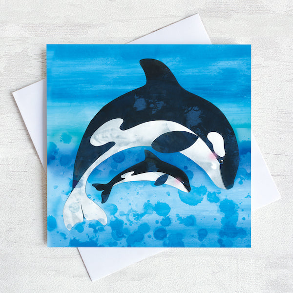 Orcas leaping on a bright blue greetings card.