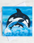 Orcas leaping on a bright blue greetings card.