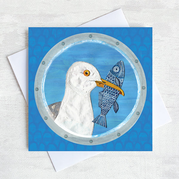 A coastal greetings card featuring a seagull with a fish in its beak.