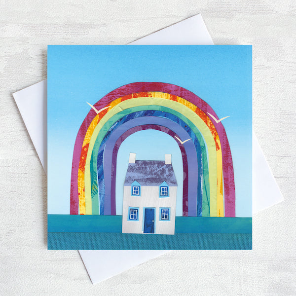 A Greetings Card featuring a white cottage with a colourful rainbow  overhead. 