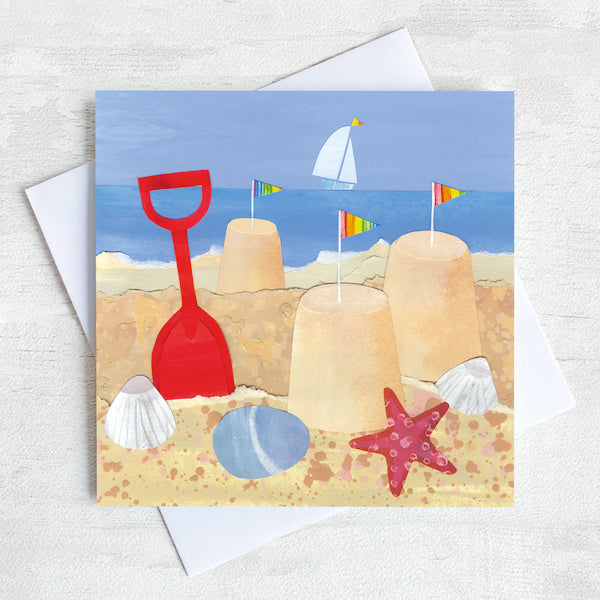 A greetings card featuring sandcastles and spade on a shore line. 