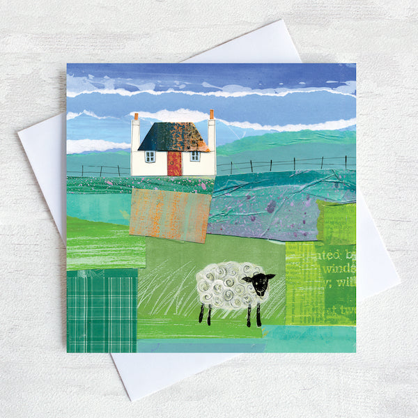 A scottish greetings card featuring a collaged artwork of a traditional blockhouse with a red door and a black headed sheep grazing in the field in front of the house.