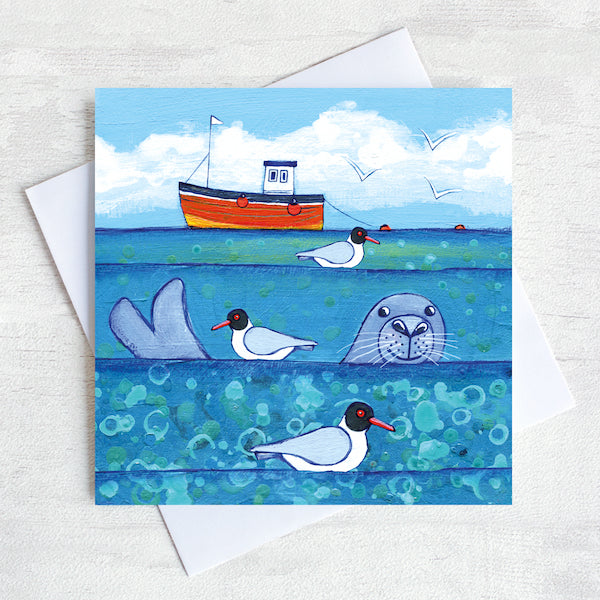 A seaside greetings card with a seals head bobbing in the sea.
