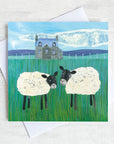 A greetings card featuring two sheep infront of a scottish stone house.