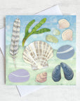 A greetings card featuring everything you may find on a beach collection. Pebbles, shells, feathers and seaweed.