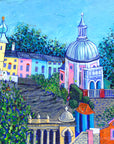 Portmeirion is an italian village on the welsh coast. In this colourful painting you can see buildings of blue green pink and yellow perched on the mountainside. The sky is blue and the buildings are interspersed with leafy green trees. 