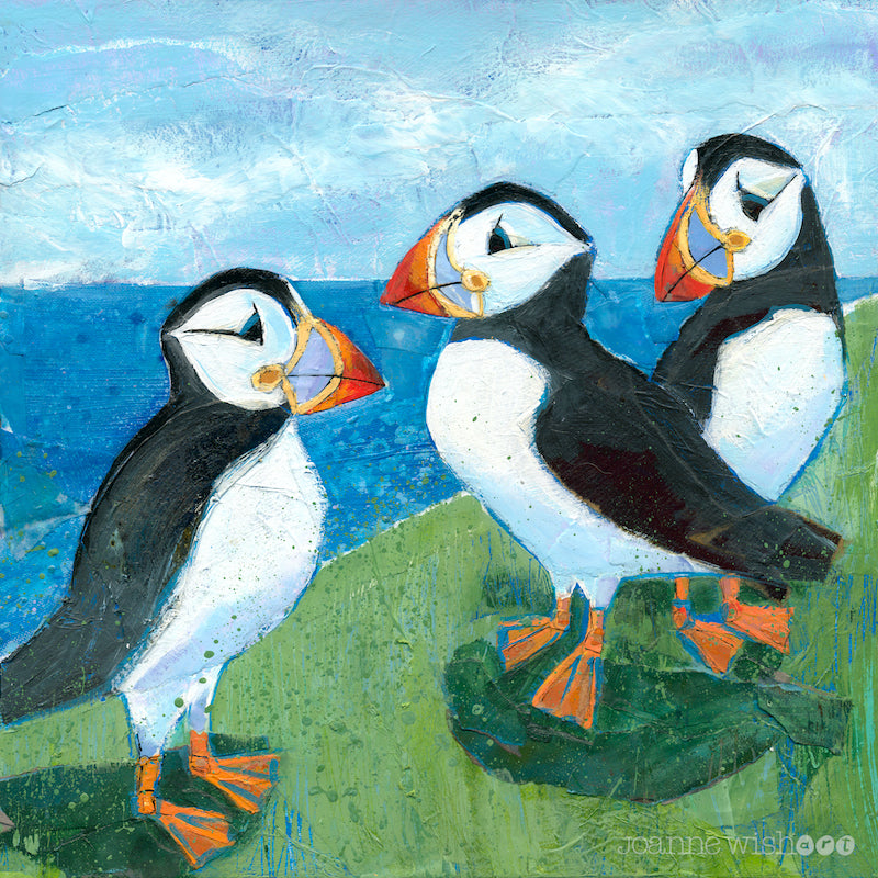 An art print of 3 cheeky puffins perched on a grassy ledge above the bright blue sea.