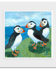 A mounted art print of three quirky puffins chatting on a grassy ledge above the north east sea.