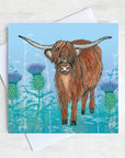 A Highland cow in the thistles on a Lavender greetings card. 